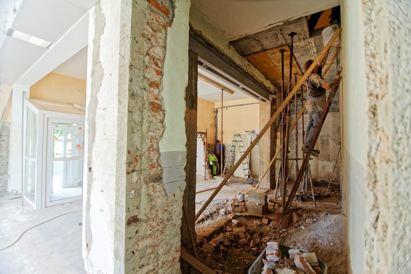 Stavební dělníci renovující budovu s odhalenými cihlovými zdmi.